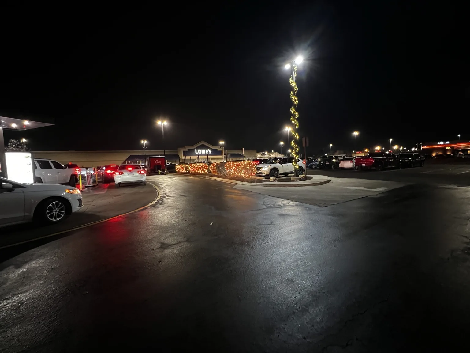 Long view across a commercial lot toward holiday roofline lights