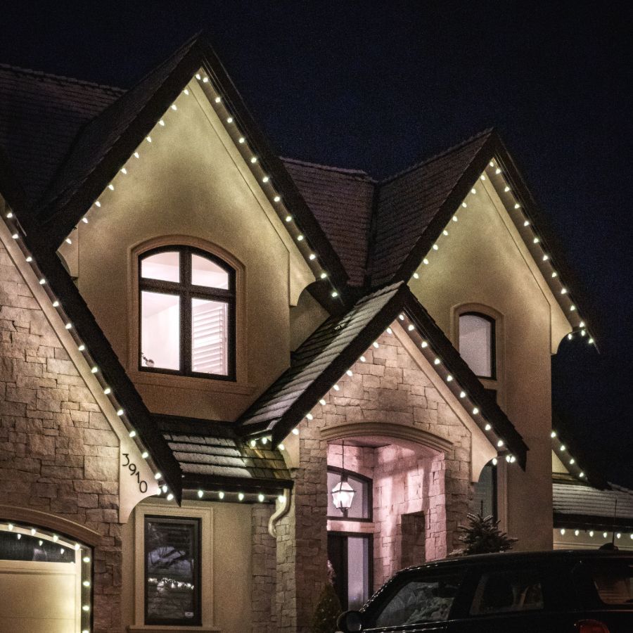 Warm white roofline lighting highlighting tall gables and a stone entryway