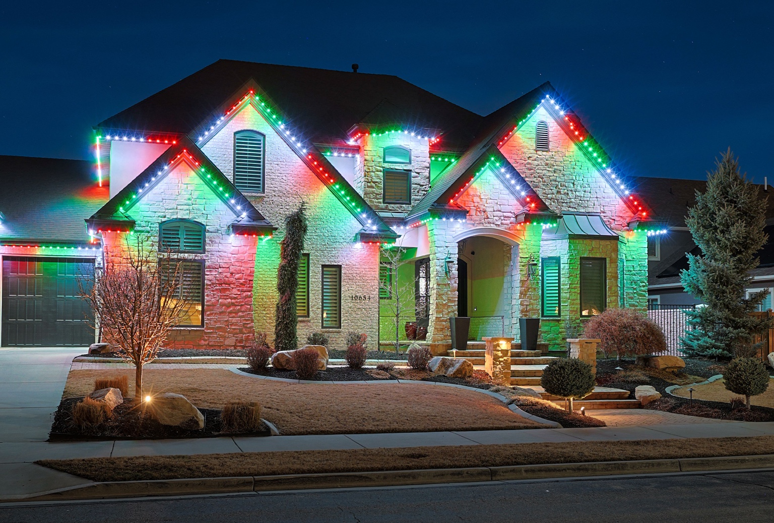 Red, green, and white lighting outlining the peaks and roofline of a two-story stone home