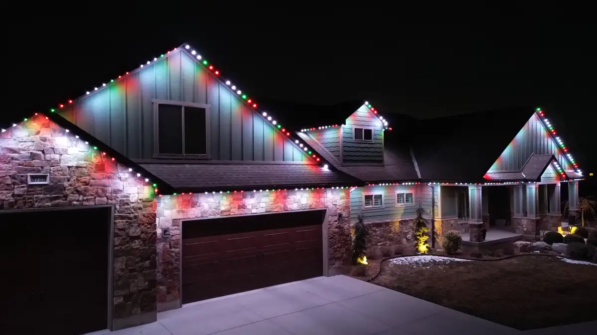 Red, green, and white roofline lighting across a home with stone garage walls and several gables