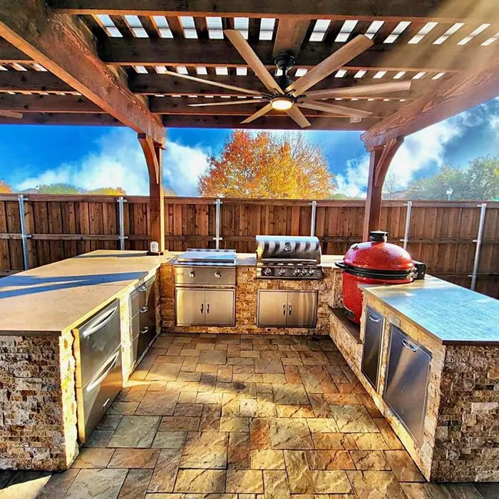 Outdoor kitchen with multiple grills beneath a pergola